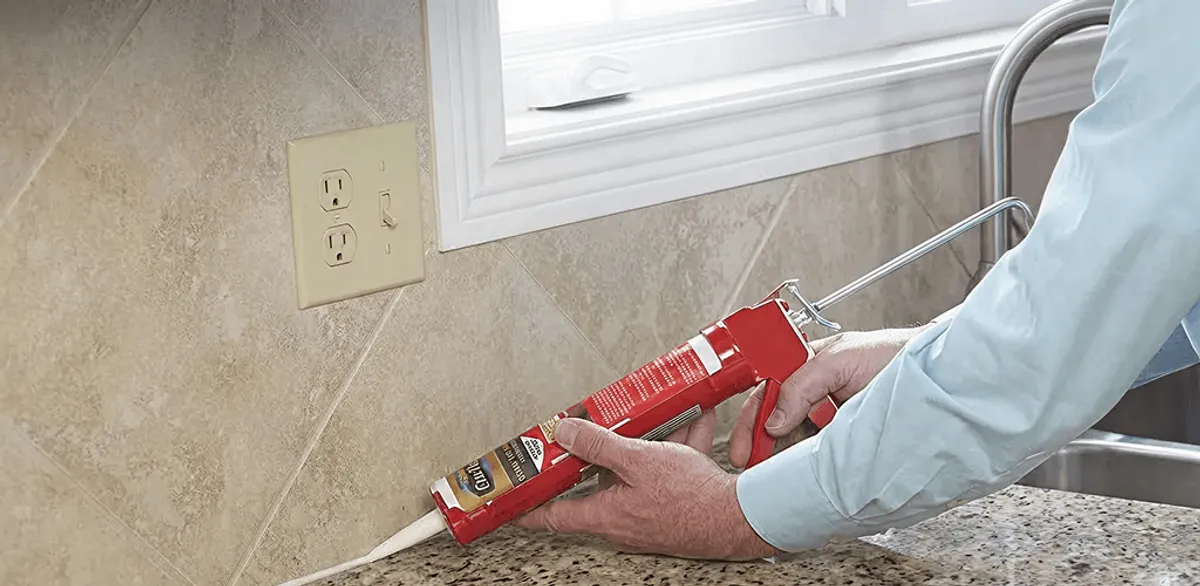 Handyman applying caulk along a kitchen backsplash and countertop seam in Overland Park, KS
